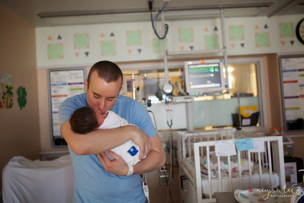Dad holding swaddled baby in NICU room during first hours together.