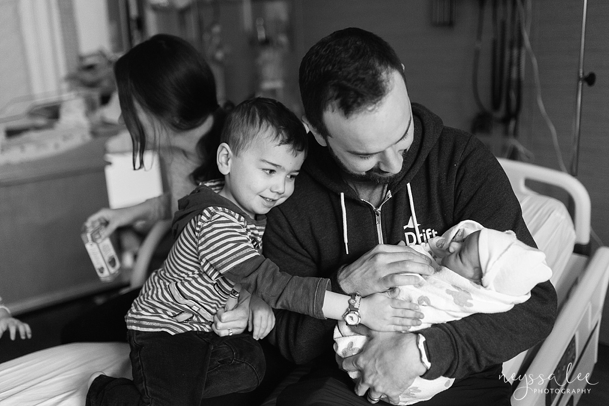 Big brother admiring new baby sister in Dad's arms