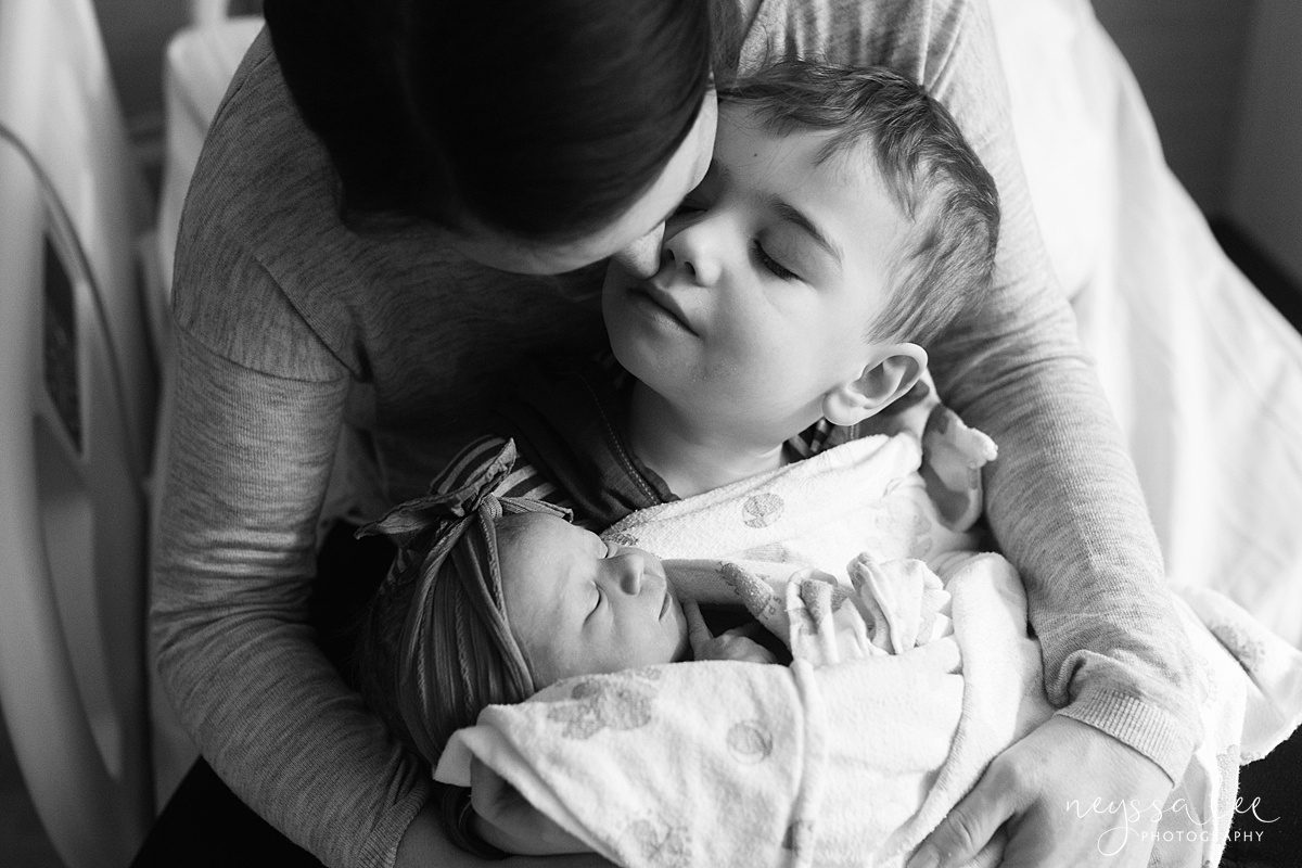 Mother kisses son on cheek while snuggling newborn baby