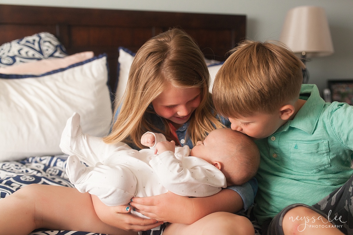 Siblings holding newborn baby, big brother kissing baby's head