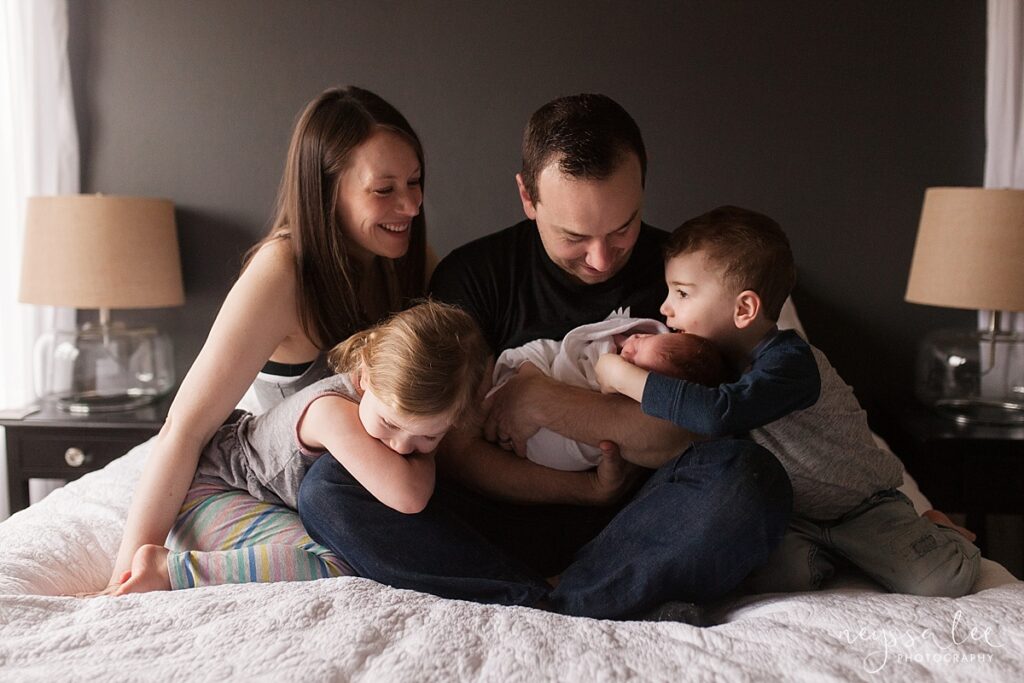 Lifestyle In-home newborn photo session of family of 5 cuddled on master bed together
