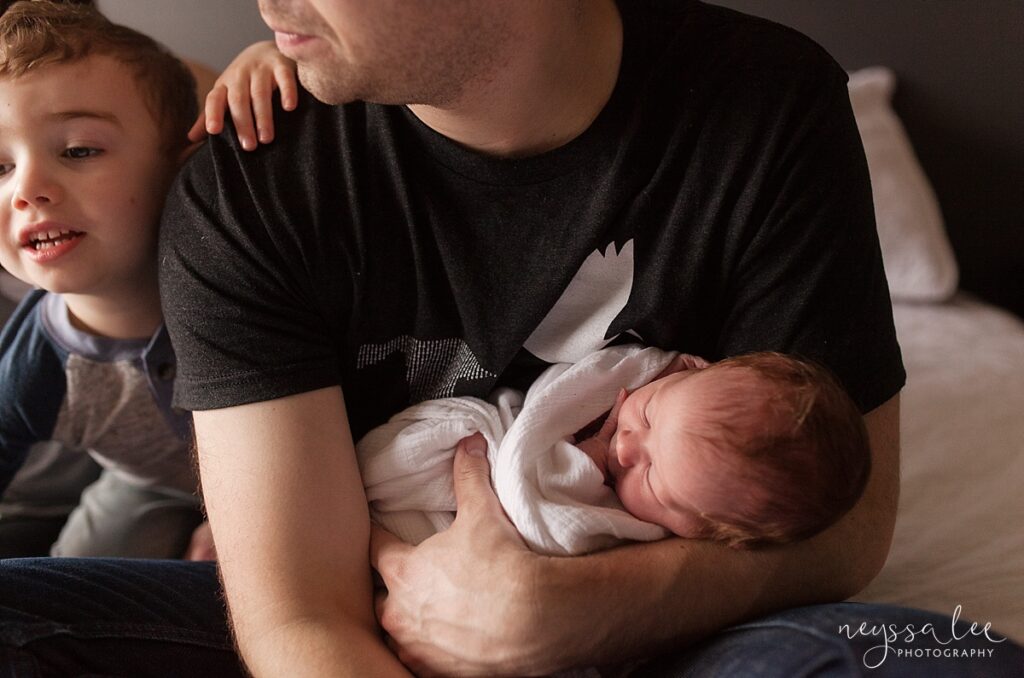 Father holding newborn baby girl with son nearby.