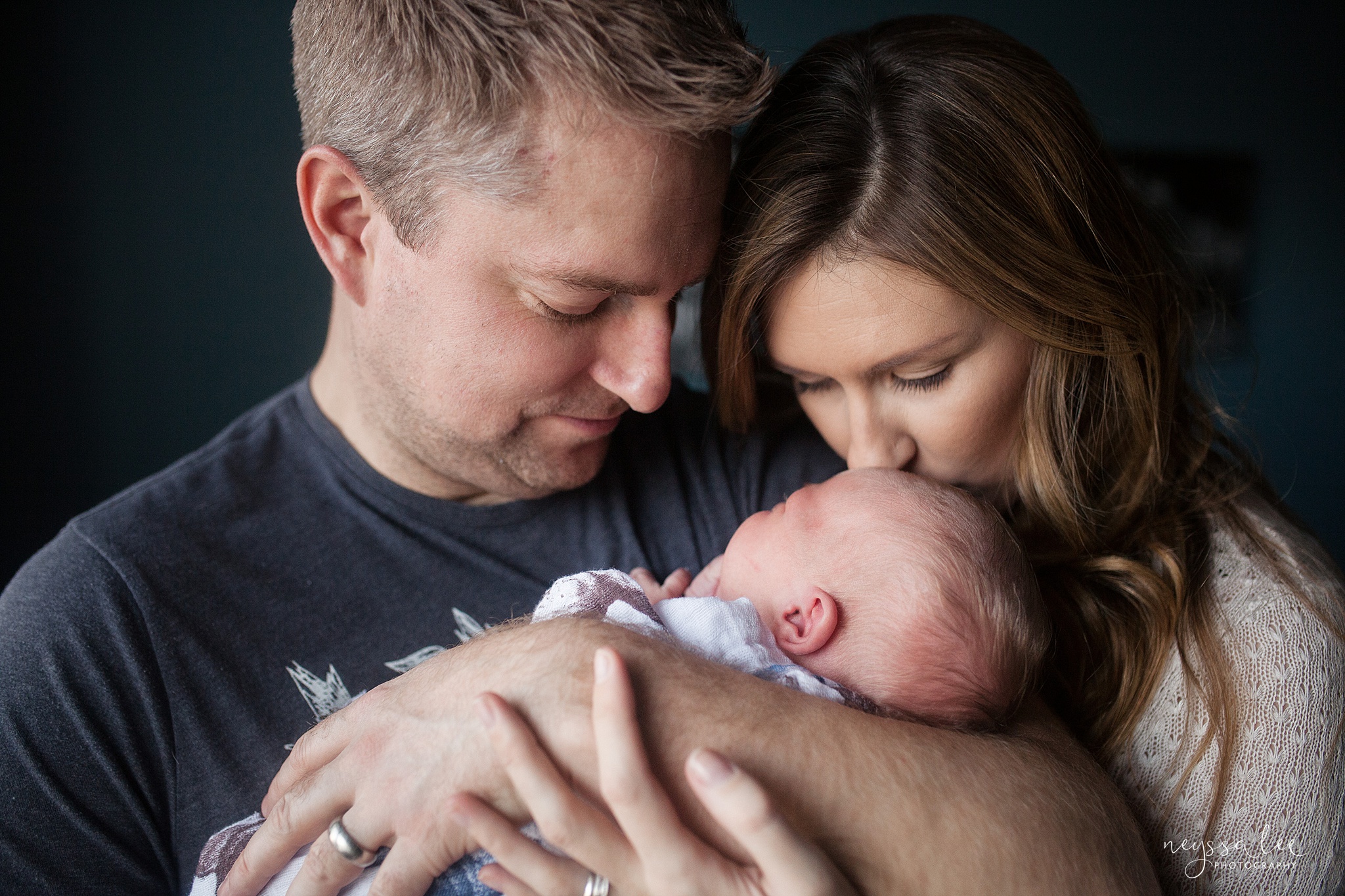 Mother kisses newborn baby boy's forehead during newborn photography session