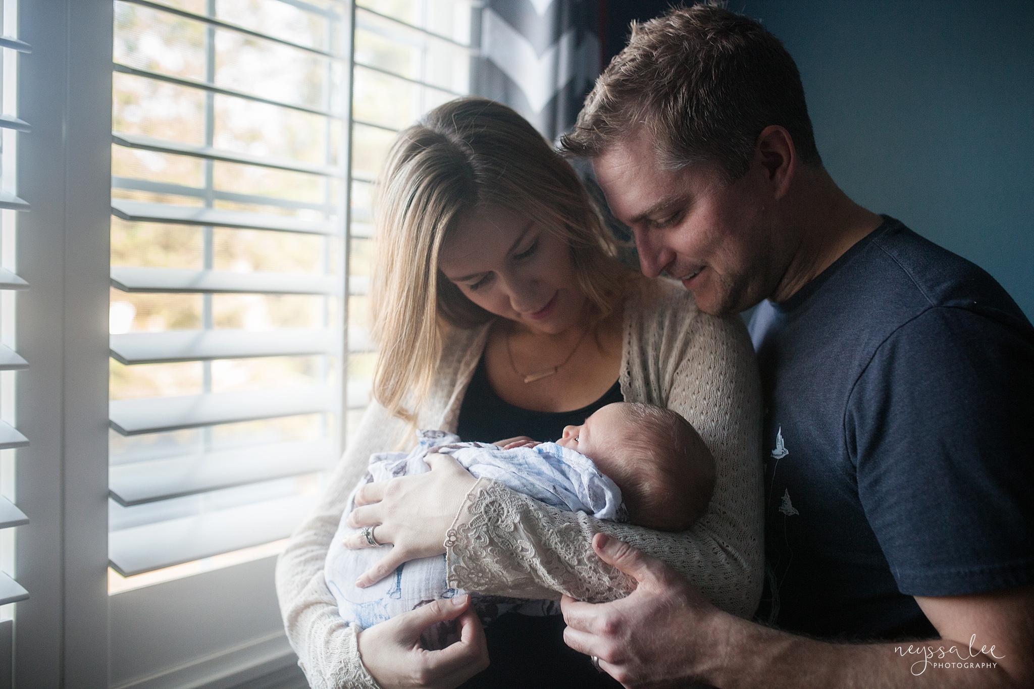 Family with newborn by window, admiring baby boy during photography session