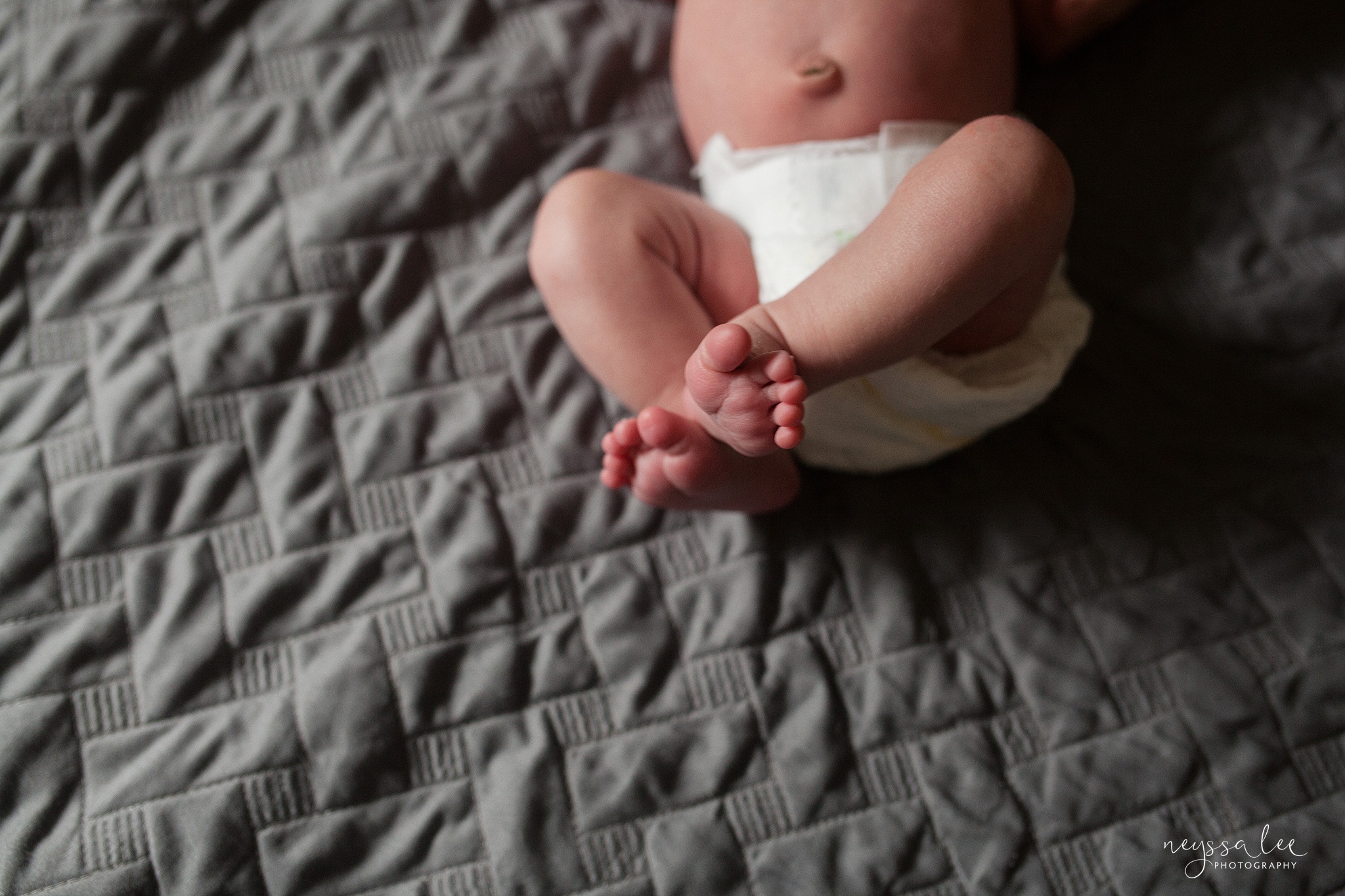 Newborn baby feet on bed, dressed in diaper