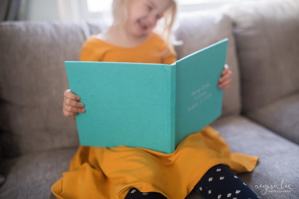 Girl in yellow dress holding teal family photo album and smiling