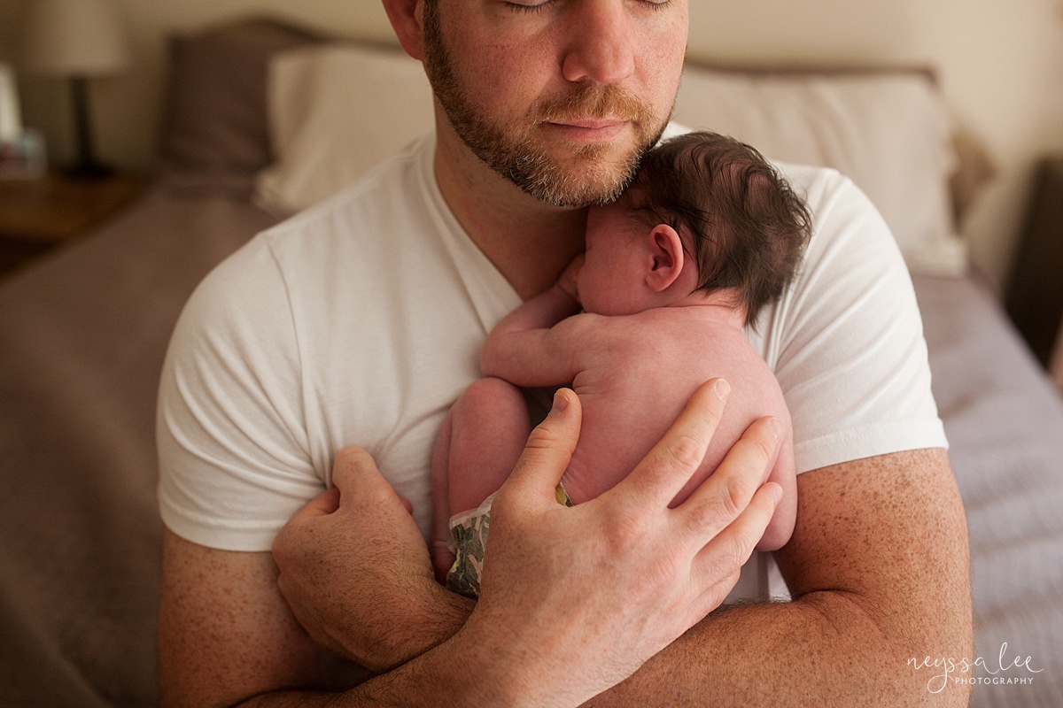  Artistic photo of dad holding newborn baby in just a diaper against his chest during Seattle newborn photography session