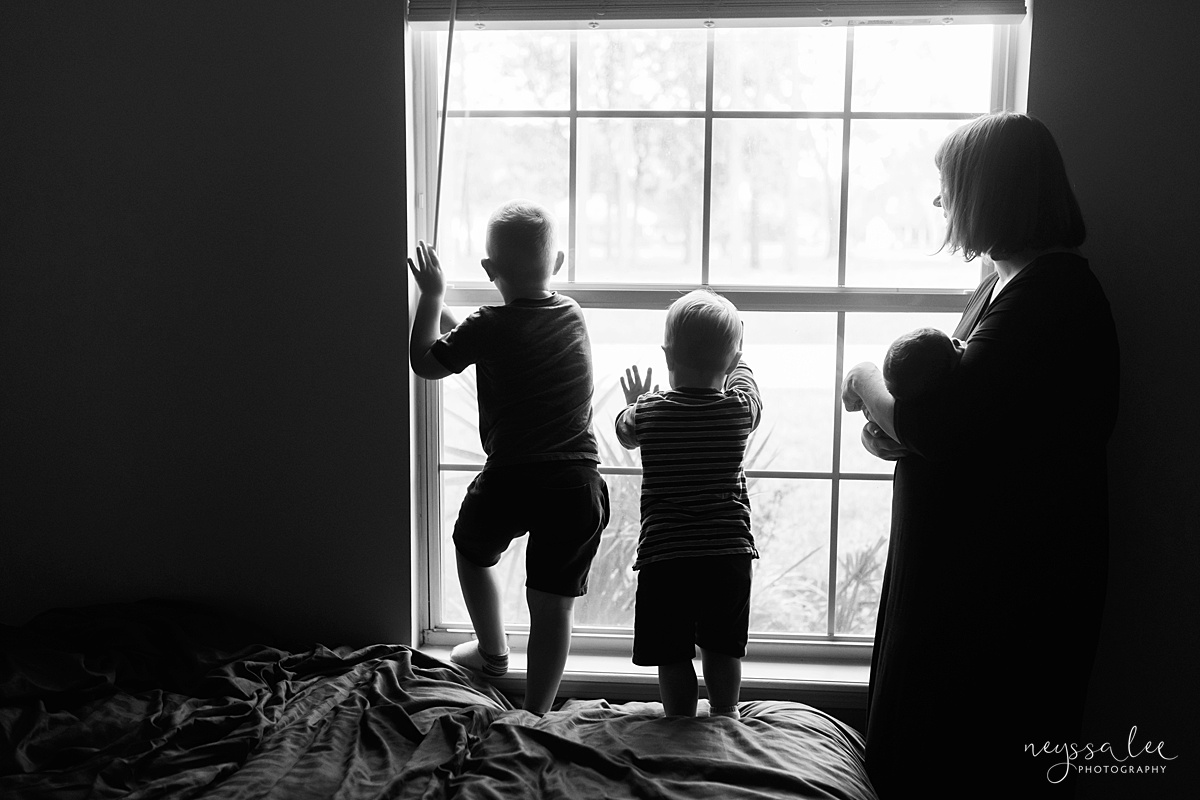 black and white photo of kids looking out window with mom and baby nearby
