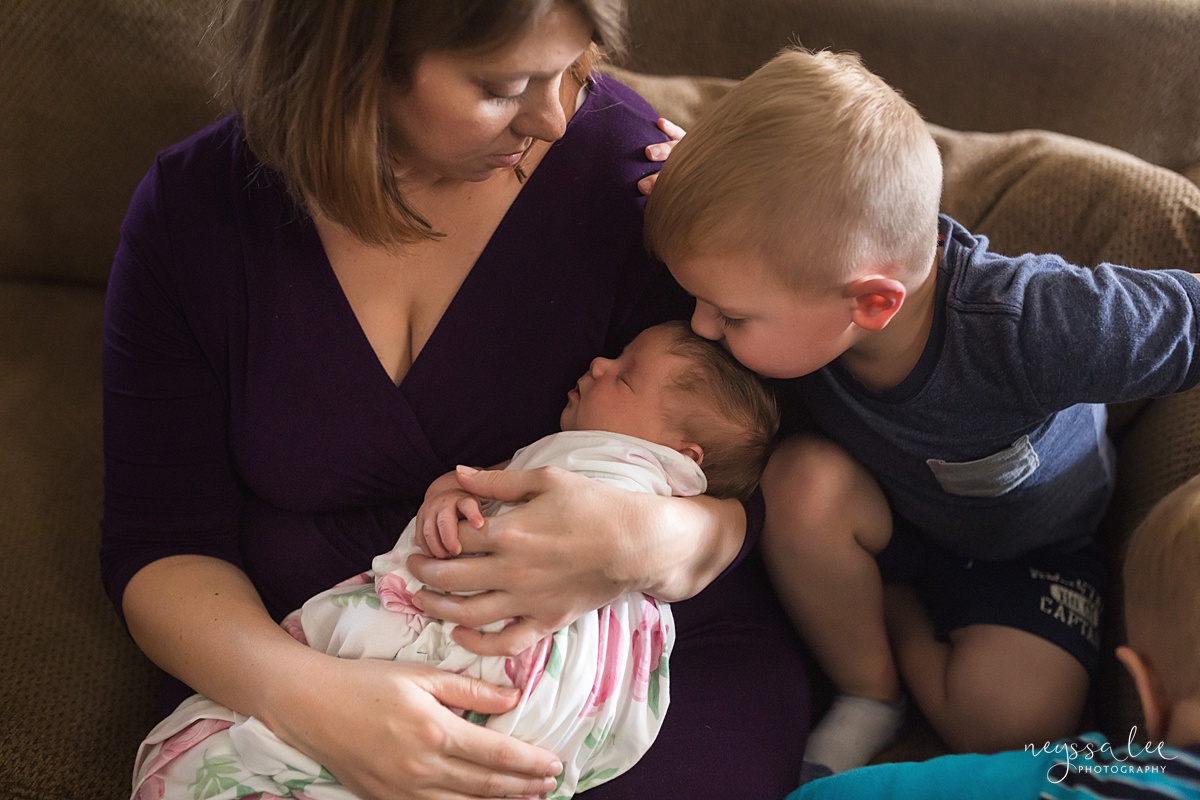 Mother holding newborn baby while little boy kisses her head during Seattle newborn photos