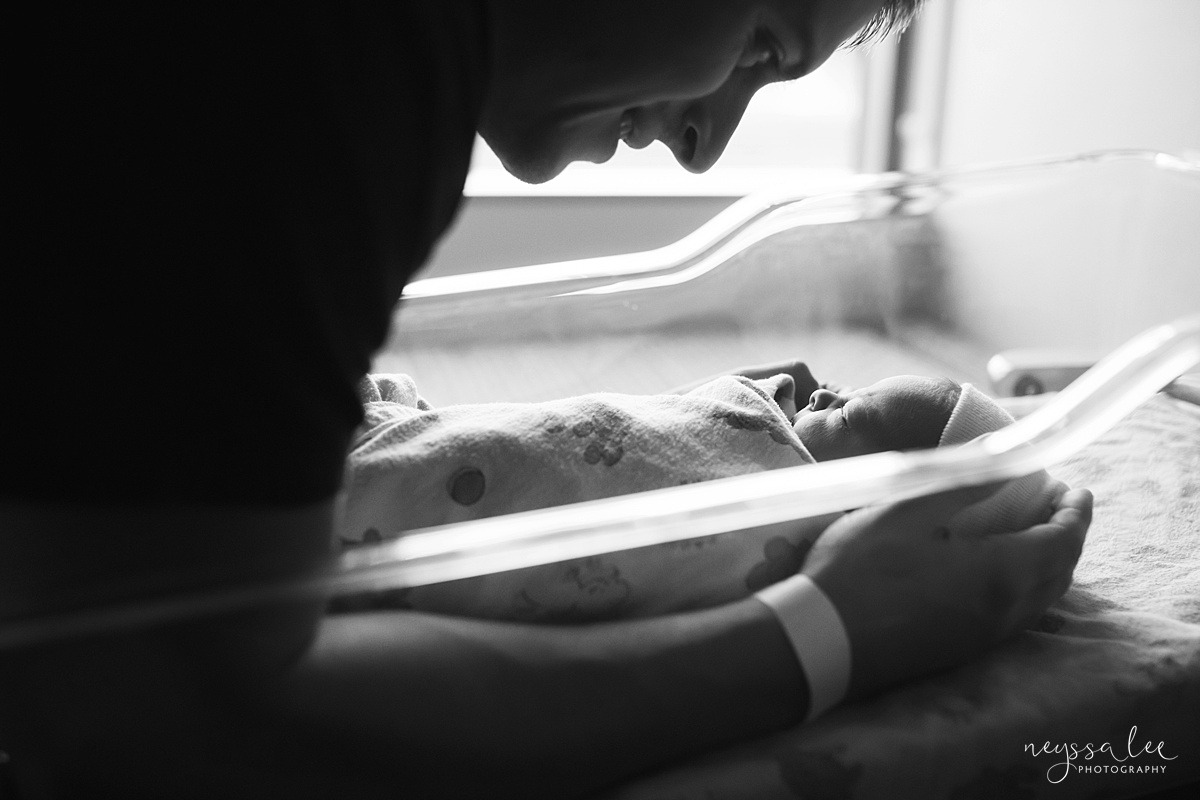 Black and white photo of dad admiring baby in hospital bassinet 