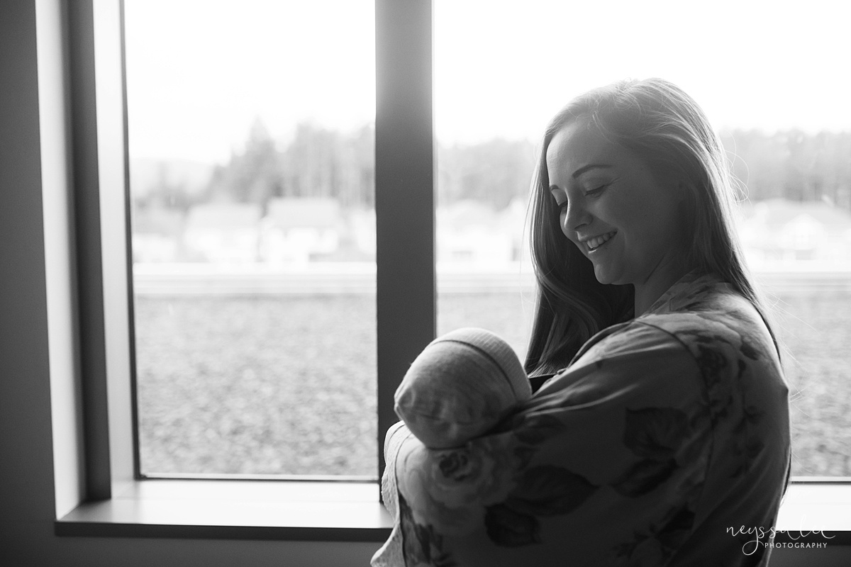 Black and white photo of mom holding newborn baby by hospital windows