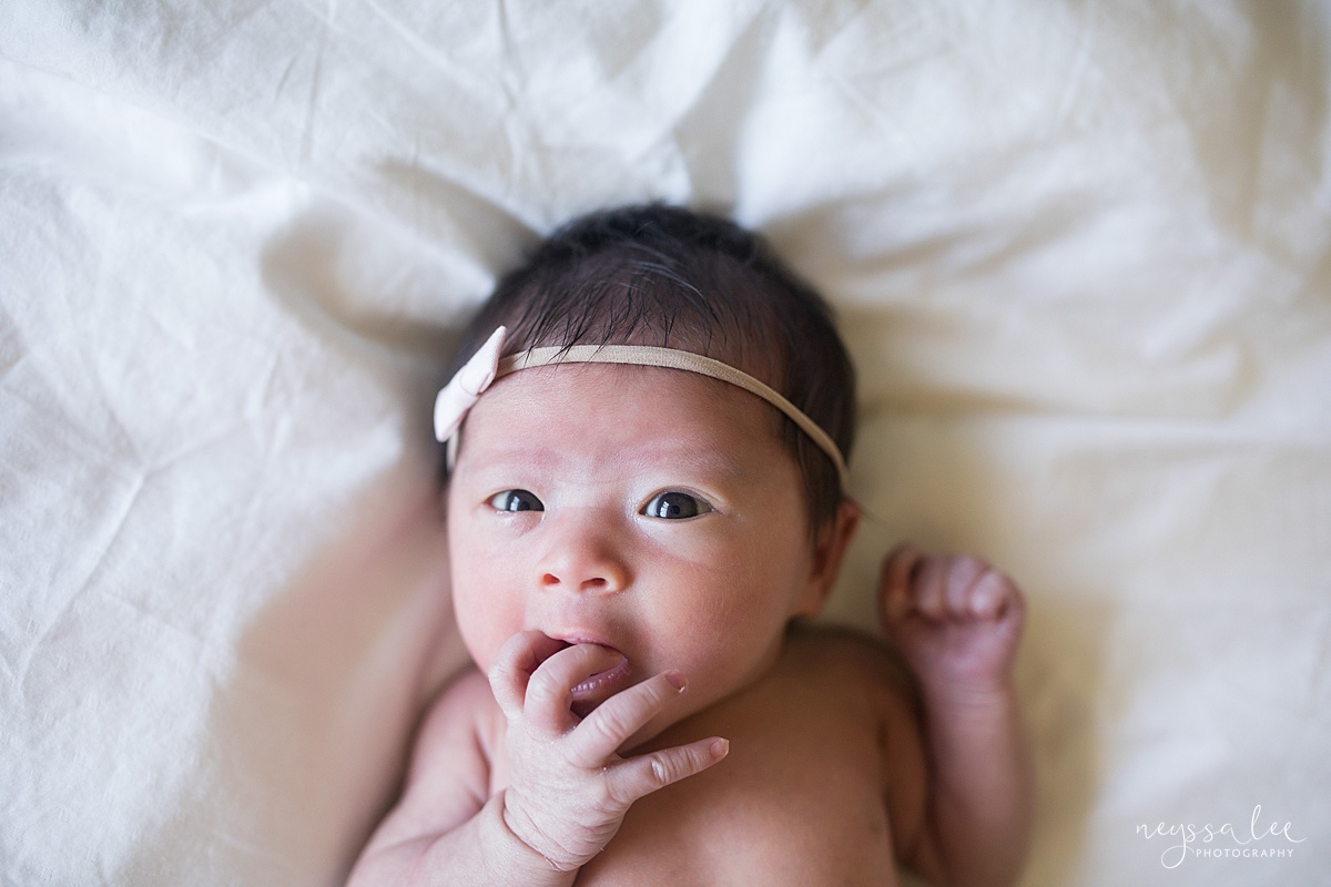 Neyssa Lee Photography, Seattle Newborn Photographer, Bellevue Lifestyle Newborn Photographer,  Photo of newborn baby with tiny bow looking at the camera