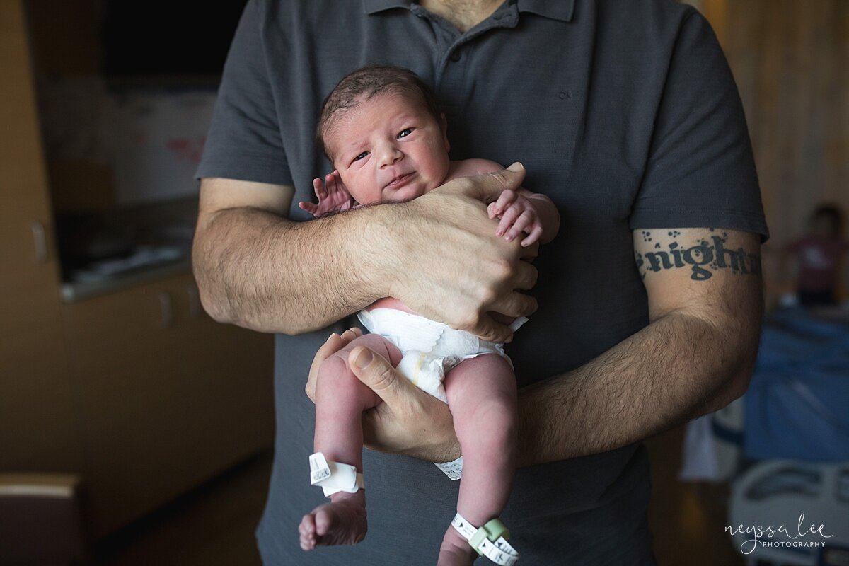 Photo of baby in diaper being held in dad's arms just hours after birth