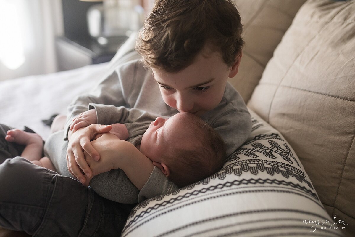 Lifestyle newborn photo of big brother holding newborn baby brother