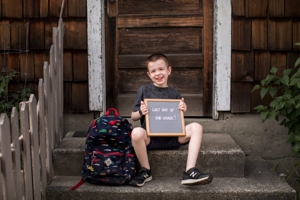 end of school year portrait of boy with letterboard and backpack