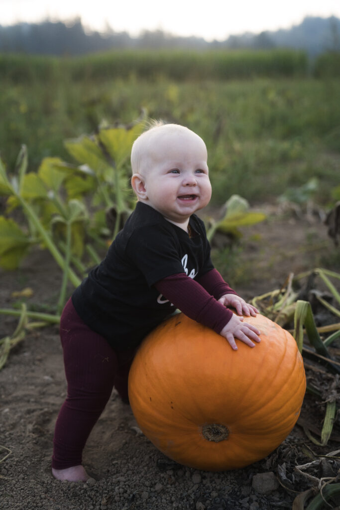 Baby standing with pumpkin for adorable pumpkin patch photo tip
