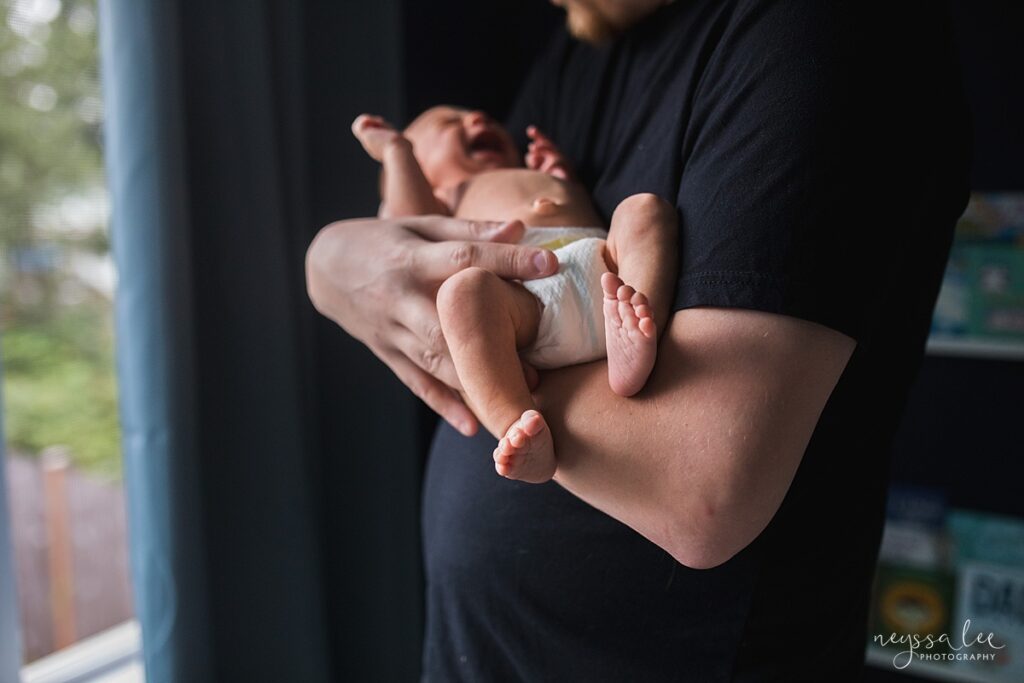 Baby in father's arms during newborn photography session in their Seattle home