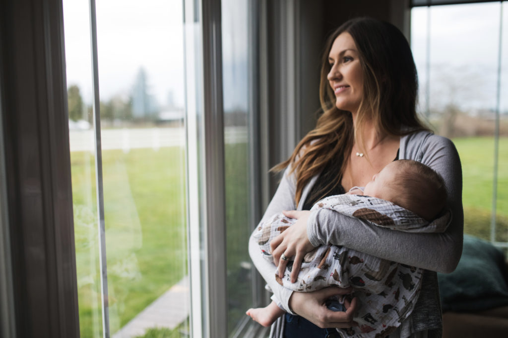 mother with newborn baby looking out window, when to take newborn photos