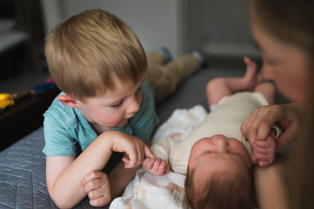big brother holding newborn baby sister's hand during in-home newborn photography session