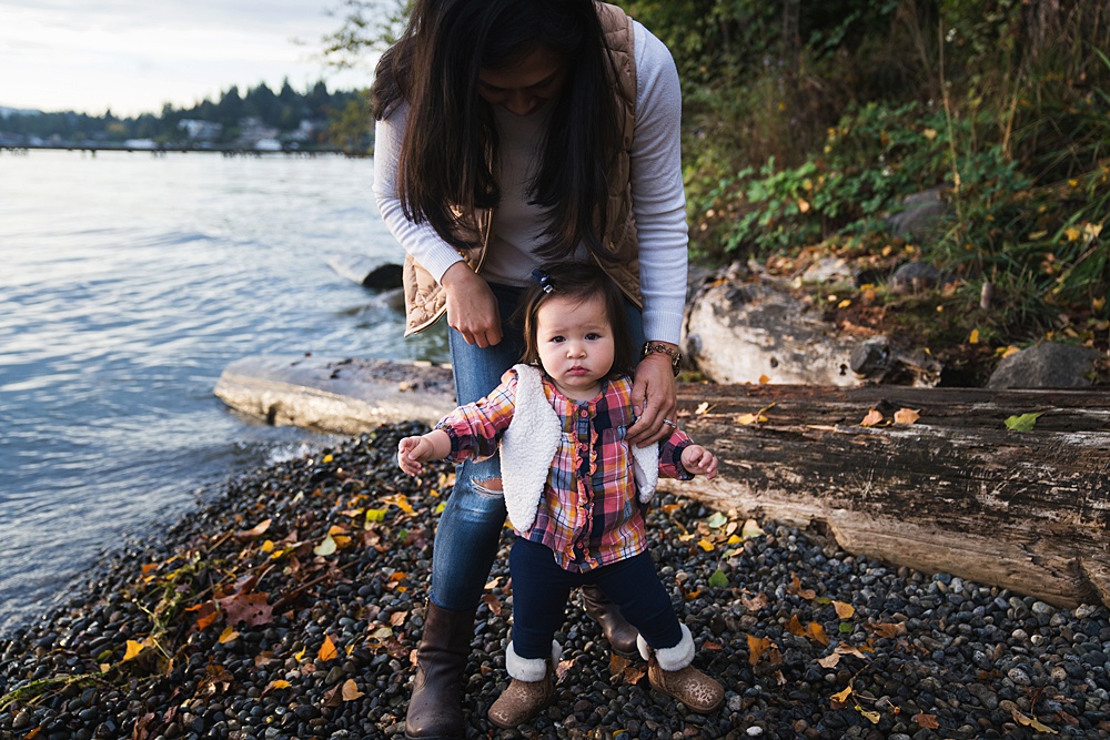 Toddler girl holding moms hands to stand on rocks