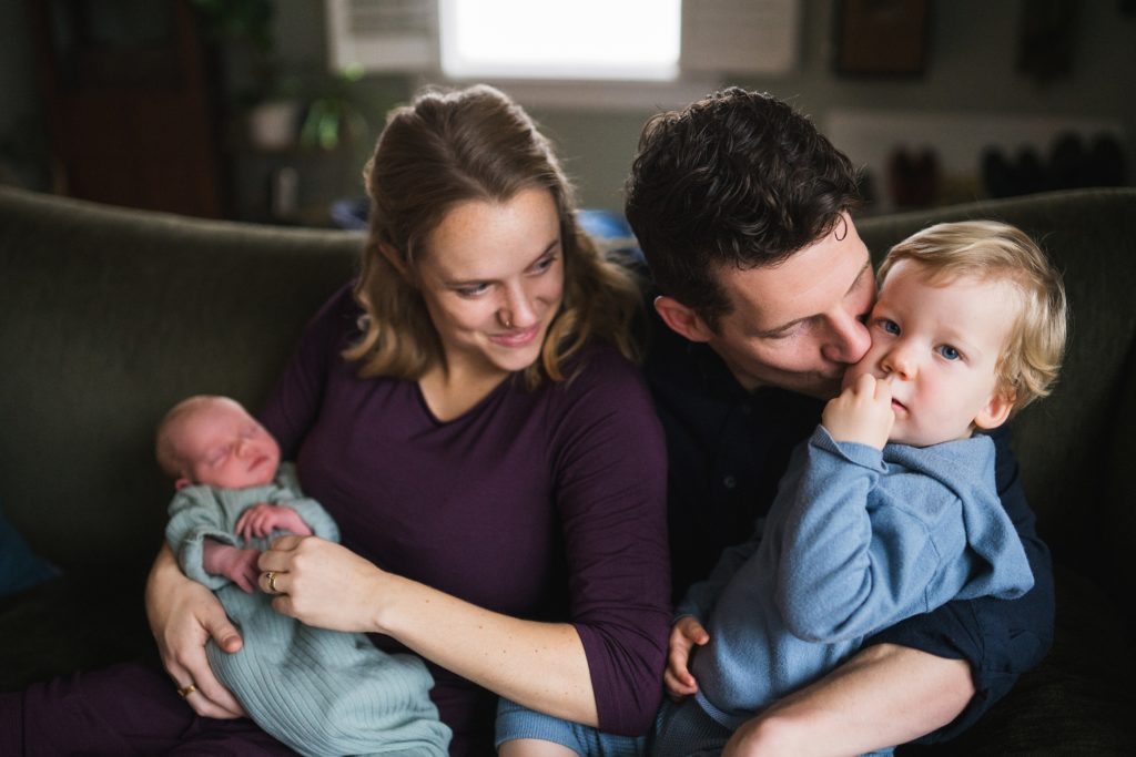 Family of four snuggled on couch with baby for Seattle area newborn photos at home