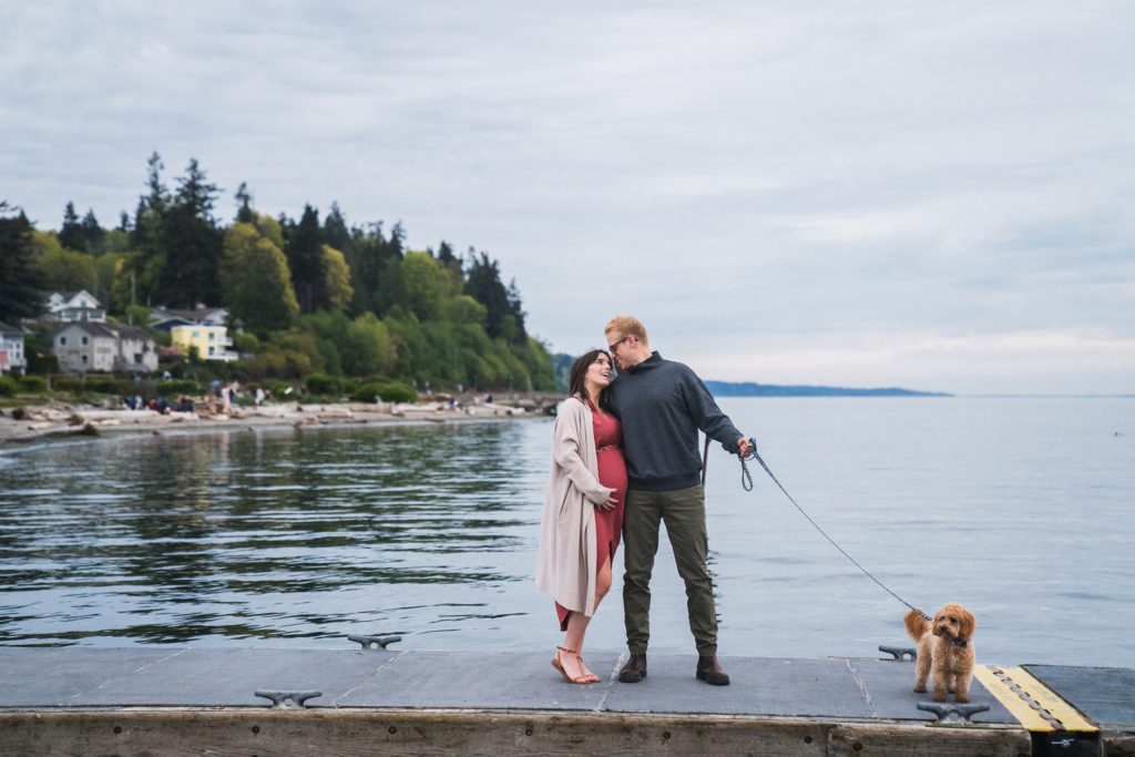 Couple standing on dock at Mukilteo Lighthouse Beach Park with dog for maternity photos