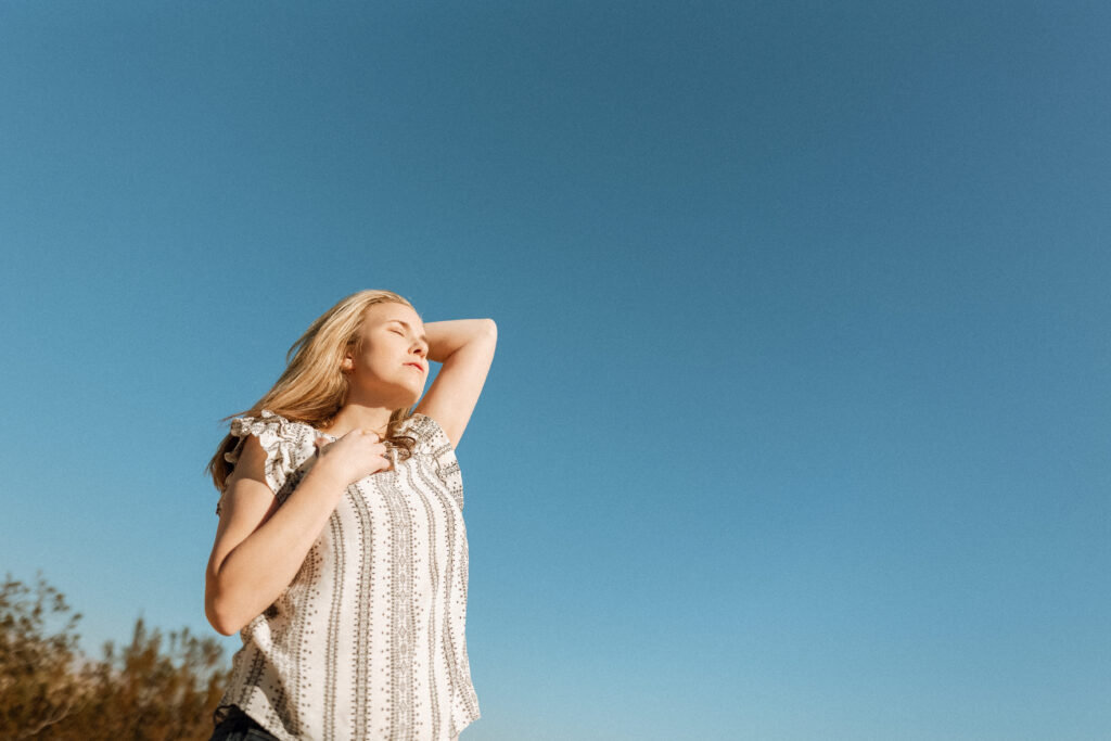 Woman breathing in, pausing, with big blue sky above her