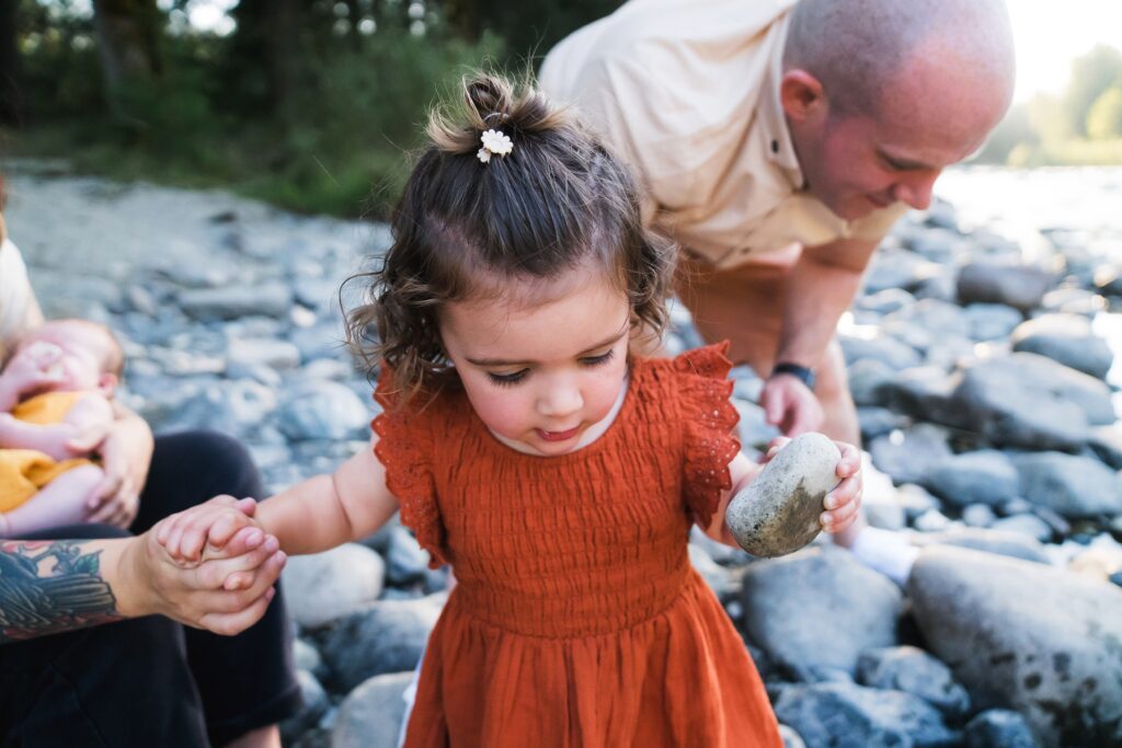 Girl holding mom's hand and rock at river during Seattle area lifestyle family photography session