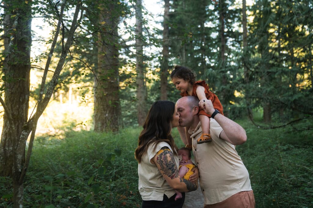 Mother and father kissing while holding girls during family photos in North Bend, WA