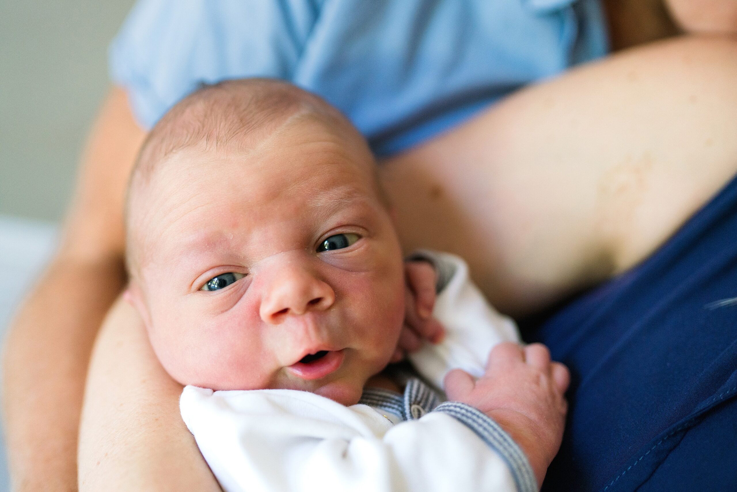 Wide-eyed, Newborn baby boy in mother's arms during in-home photography session