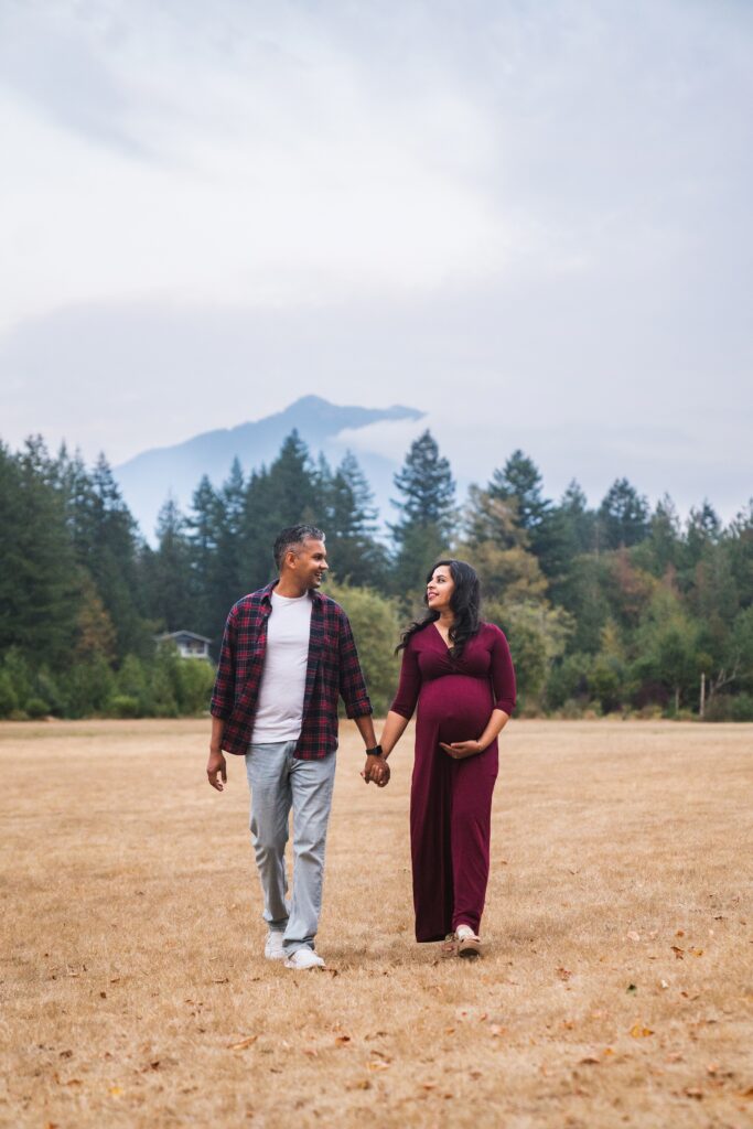 Best time for outdoor maternity pictures show with couple walking with mountains behind them