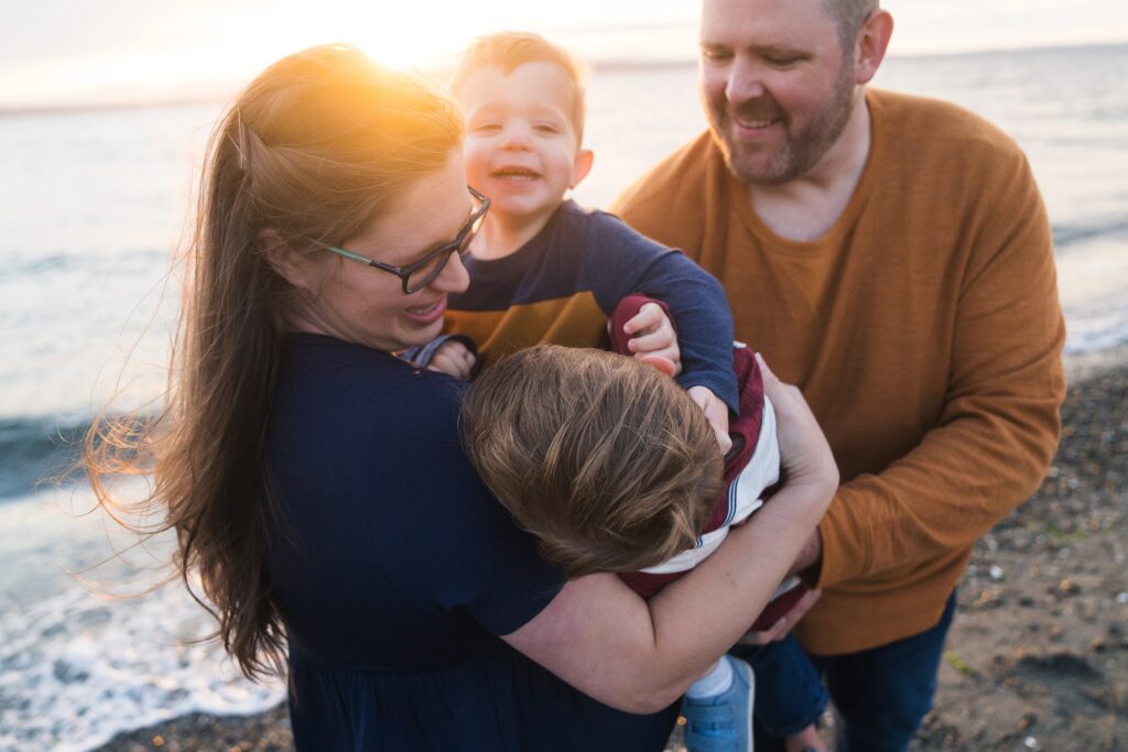 Family of four laughing and hugging during maternity photo session in Seattle at sunset