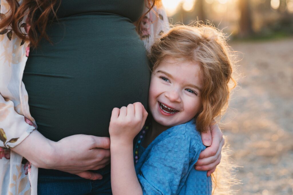 Young girl hugging mom's baby bump during  outdoor maternity portrait session