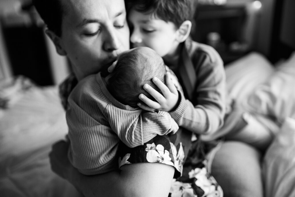 Black and white portrait of father holding newborn baby with boy snuggling in close