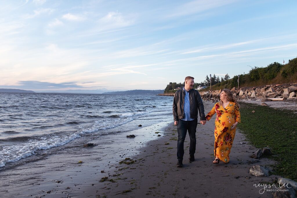 Spring maternity shoot with a woman in a yellow floral dress walking on the beach at Bracett's Landing North in Edmonds, Wa