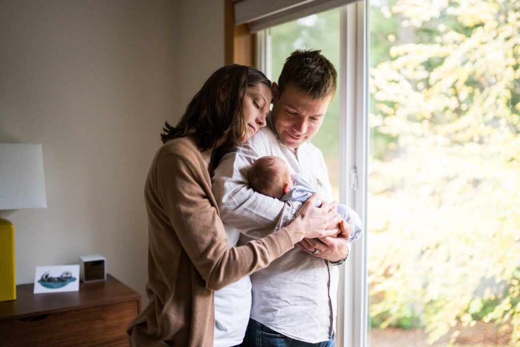 Relaxed in-home newborn portrait session of parents by window cuddled together