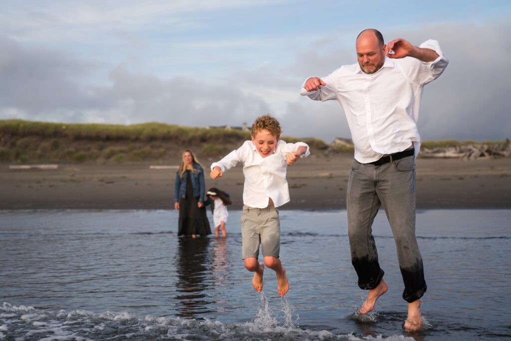 father and son jumping waves during portrait session at Ocean Shores, WA