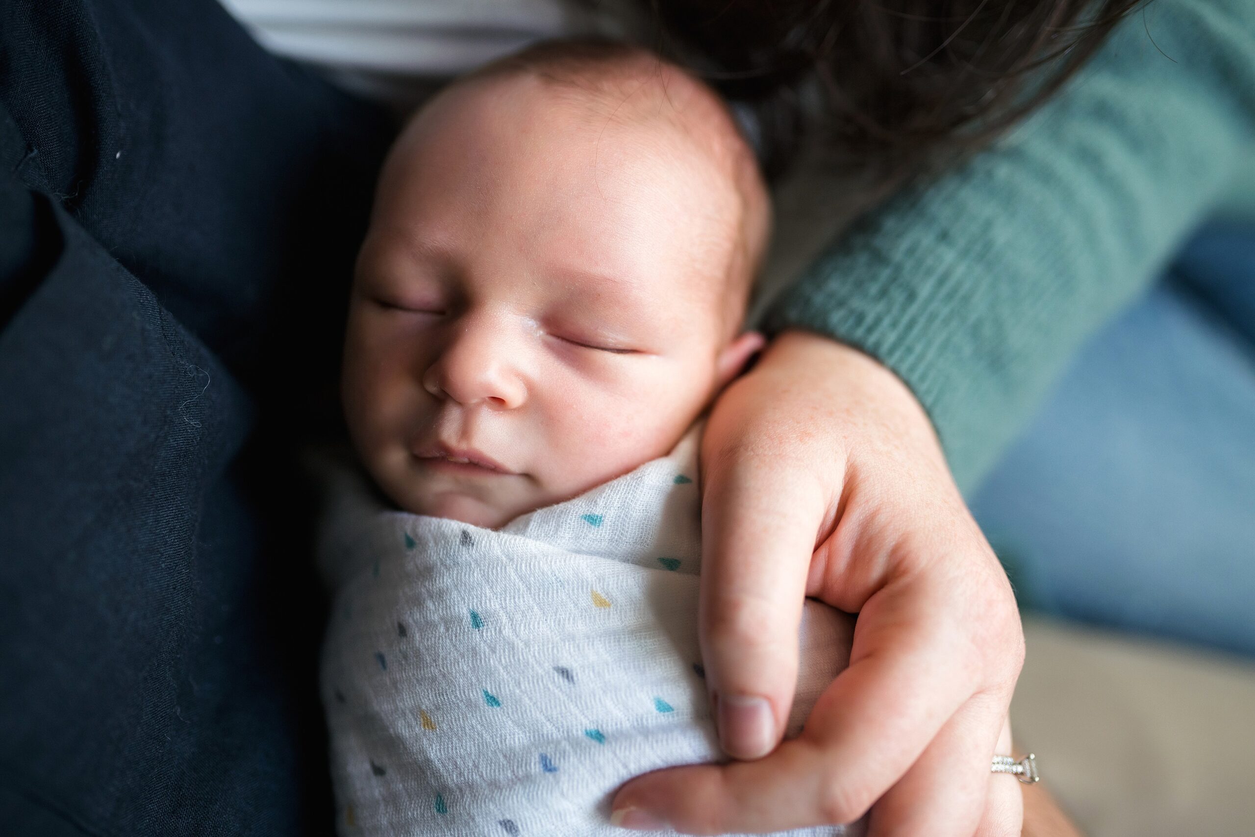 Swaddled newborn baby in parents arms during in home newborn photo session