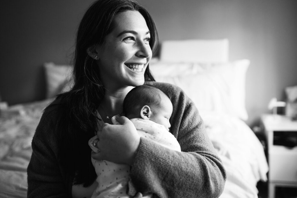 Black and white photo of mother smiling while holding baby during Seattle portrait session
