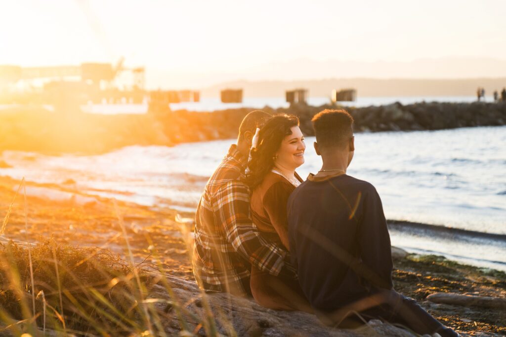 Family snuggled on a log at a Seattle beach at sunset