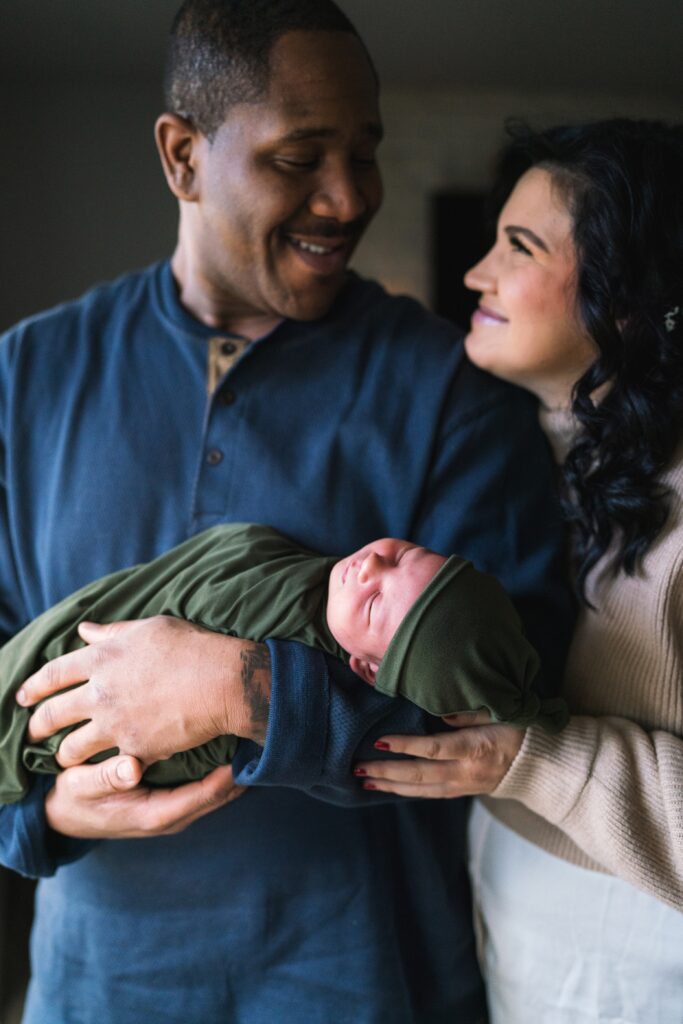 Seattle  lifestyle newborn photo of husband and wife smiling at each other while holding newborn boy