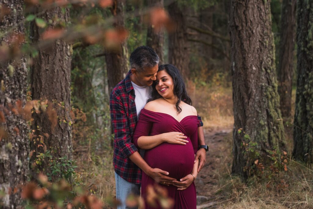 What to wear for fall maternity photos example of couple in burgundy in the woods in Seattle