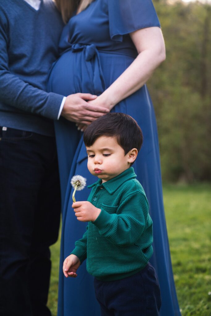 Boy blowing dandelion flower in front of parents during Seattle maternity photoshoot