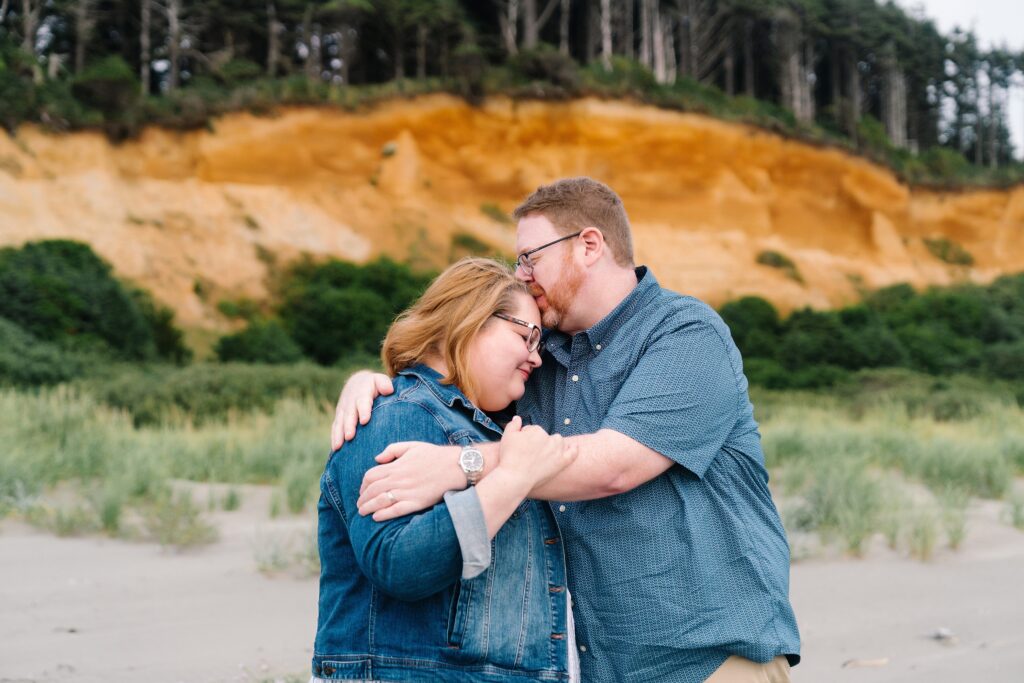 Husband and wife embracing with beautiful red rock hillside behind them, Seabrook, Wa