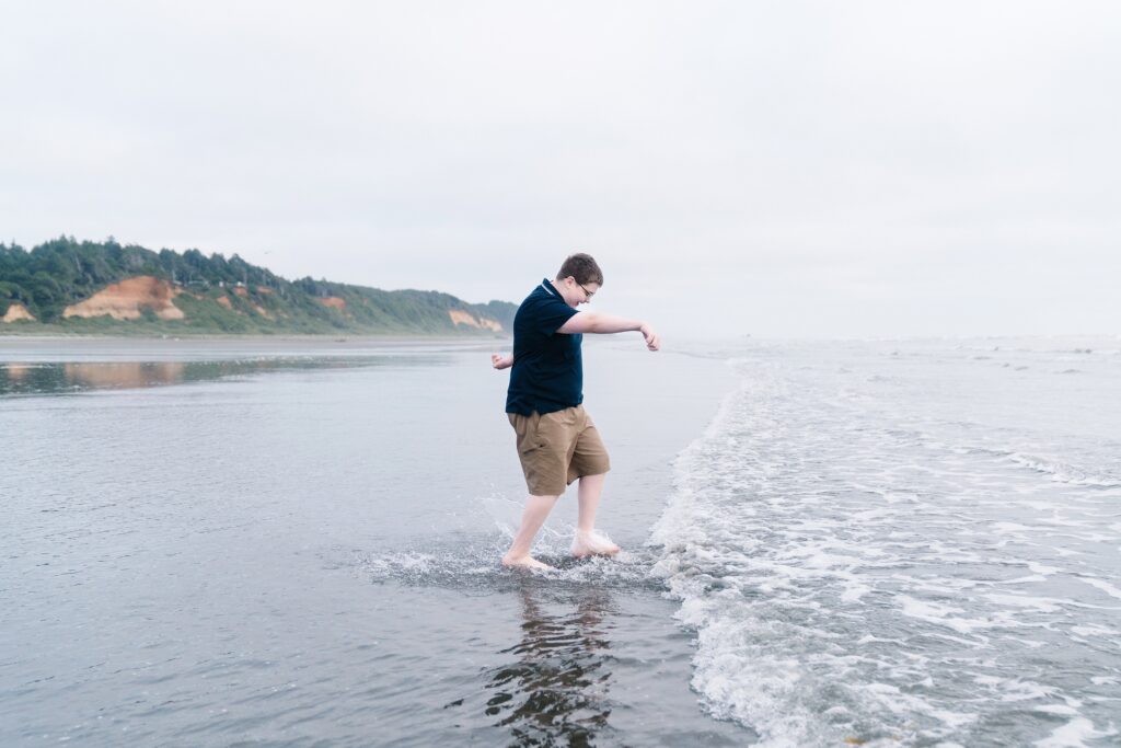 Boy kicking the waves during family photos at Roosevelt Beach, WA