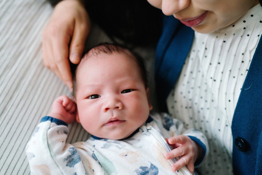 Newborn baby boy looking at camera with mom surrounding lovingly during Seattle in home newborn photography photoshoot