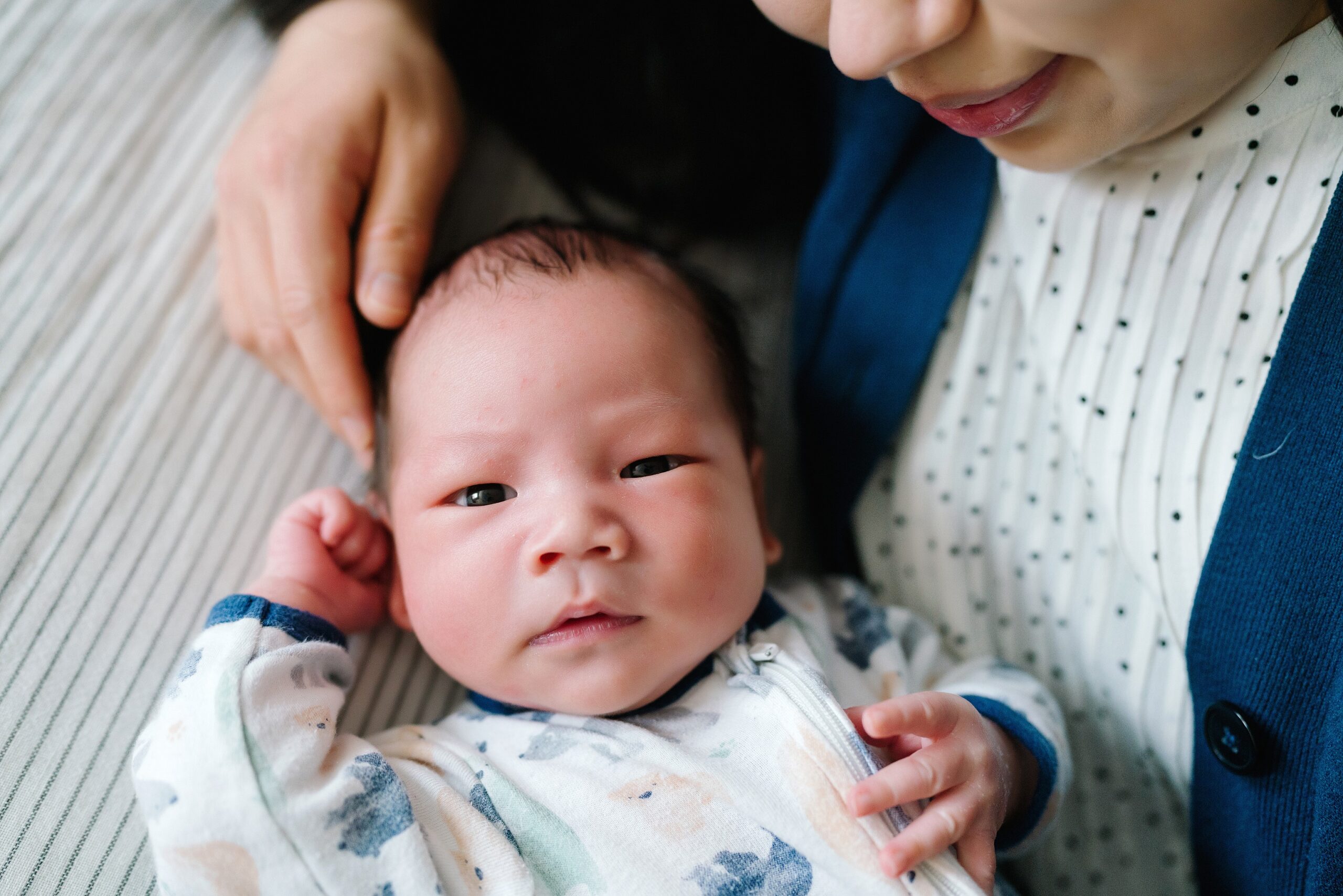 Newborn baby boy looking at camera with mom surrounding lovingly during Seattle in home newborn photography photoshoot