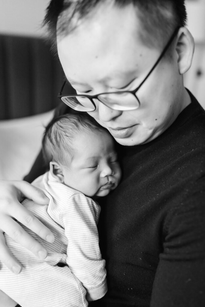 black and white photo of father holding newborn baby boy against his chest during Seattle in home newborn photos