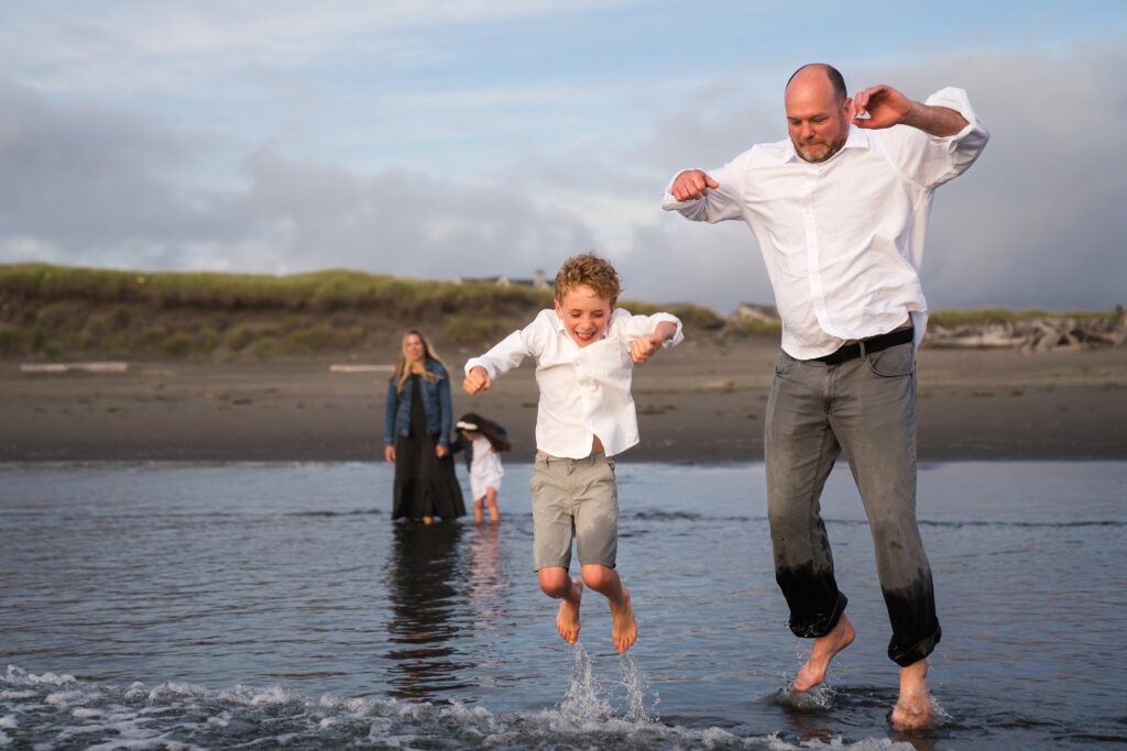 Father and son jumping waves in Seabrook, Wa during family photos