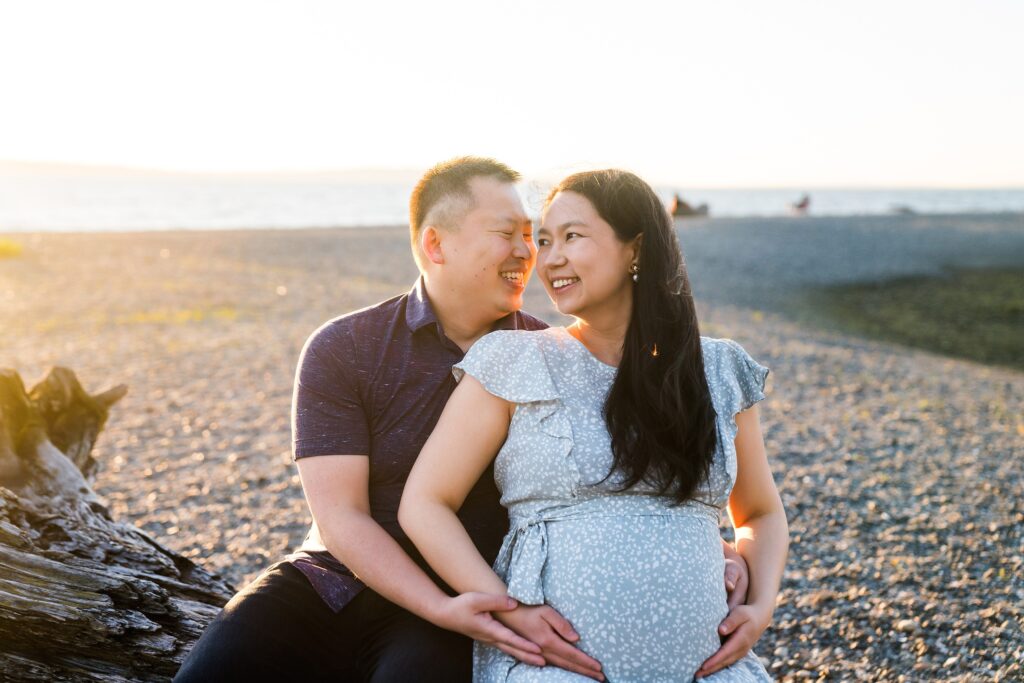 Couple sitting on log together during Seattle beach maternity photoshoot